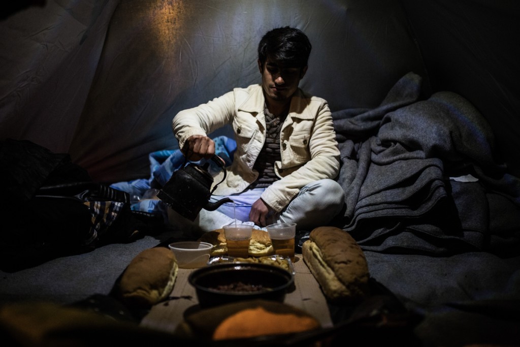 Mohammed Abdul from Afghanistan fills a plastic glass with tea as before a dinner with his friends inside a tent at the refugee camp at the Greek - FYROM border near the village of Idomeni on March 11, 2016.